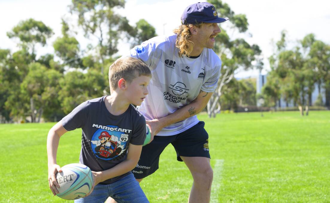 Ben O'Donnell passes with young fan Mason Kerr at Sunday's ACT Brumbies fan day. Picture by Keegan Carroll