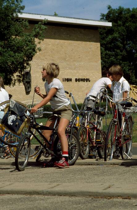 Year 7 students jump on their bikes after a long day at Watson High, 1982. Image courtesy of the National Archives of Australia. A6135, K23/11/82/2