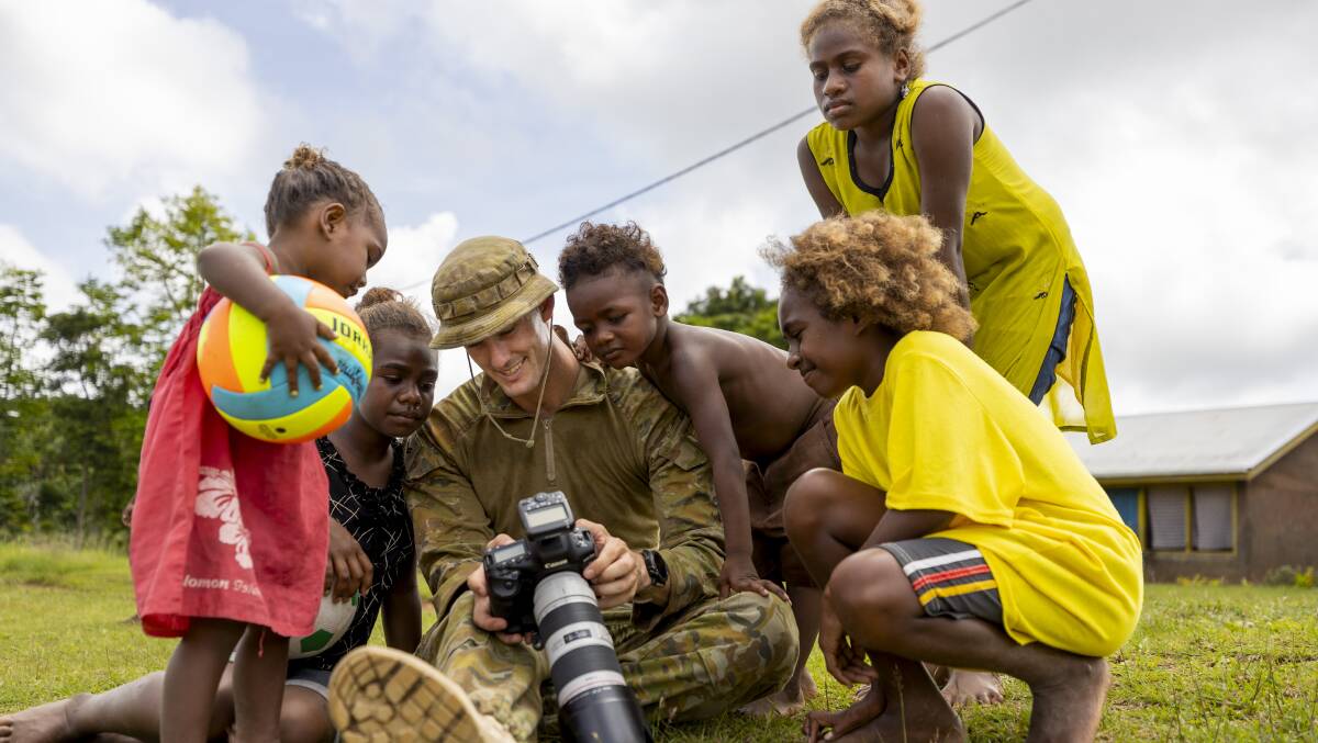 Australian Army soldier Corporal Brandon Grey deployed on Operation Lilia shows children photographs on his camera at the Private Jamie Clark Memorial Kindergarten in Honiara, Solomon Islands. Picture Defence
