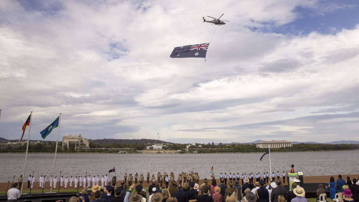 A MH90 Seahawk flies over the proceedings carrying the Australian flag. Picture: Keegan Carroll