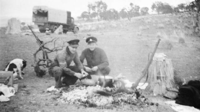 Two RAAF personnel on guard duty at the crash site cook breakfast over the remains of a bonfire, which would have provided heat during the cold nights. Picture: Australian War Memorial