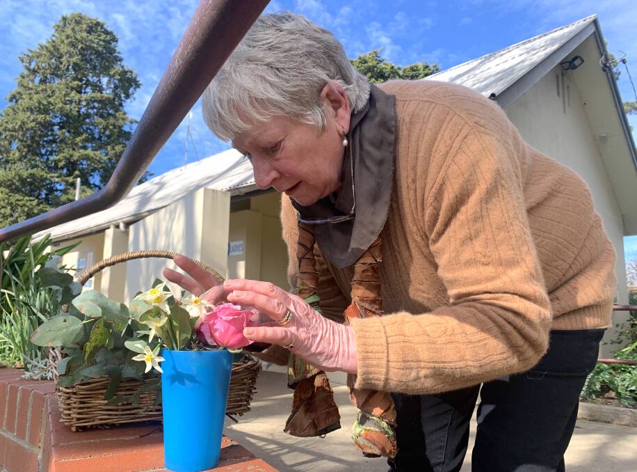 Margaret Tuckwell, aka the Flower Fairy, arranges flowers in a plastic vase outside the public toilets in Braidwood Memorial Park. Picture: Tim the Yowie Man