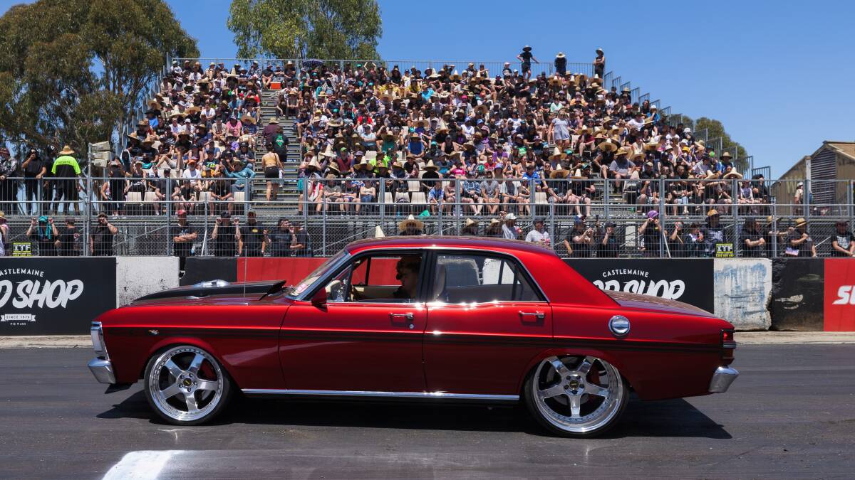 An XY Ford Falcon in candy apple red paintwork cruises past the packed grandstand at the Summernats burnout pad. Picture by Sitthixay Ditthavong