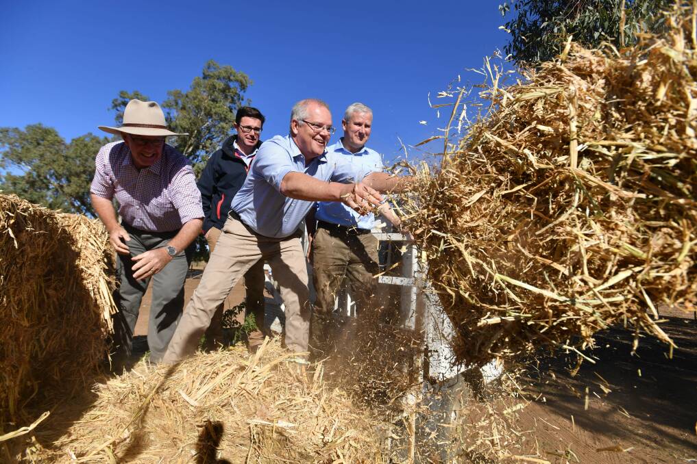 Prime Minister Scott Morrison, Deputy Prime Minister Michael McCormack and Minister for Agriculture David Littleproud throw hay to feed cattle on Eumungerie Farm. Picture: AAP