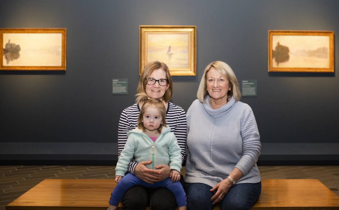 Afton Bell (left) with her daughter Lucy, 18-months, and her mother Vicki Gooda at the National Gallery of Australia's most recent exhibition, Monet: Impression Sunrise, in front of The Seine at Port-Villez, pink effect 1894; The sailing boat, evening effect 1885; and The Seine at Port-Villez, evening effect 1894. Picture: Jamila Toderas