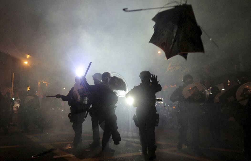 A broken umbrella flies near riot police during a confrontation with protesters in Hong Kong. Below: protesters shine lasers at police and facial recognition cameras. Picture: AP