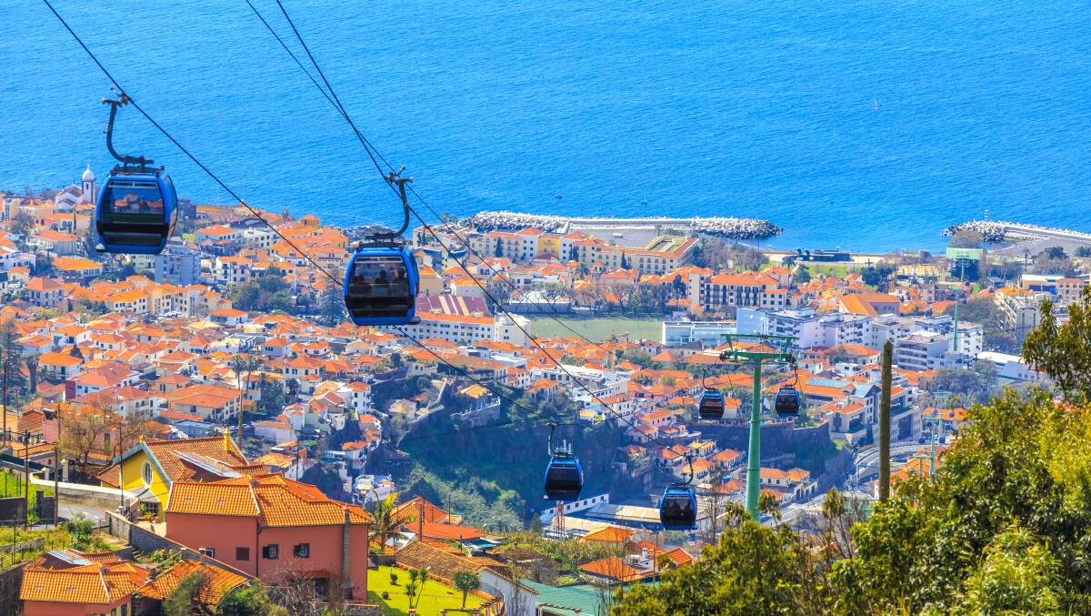 Overhead cable cars transport tourists above Funchal city in Madeira.