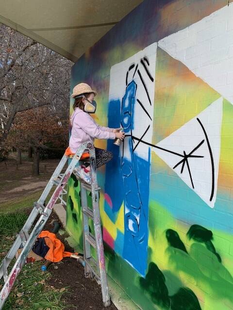 Lucy Filmer, 8, adds her touch to the Floriade mural being painted in Commonwealth Park by her dad and grandparents.