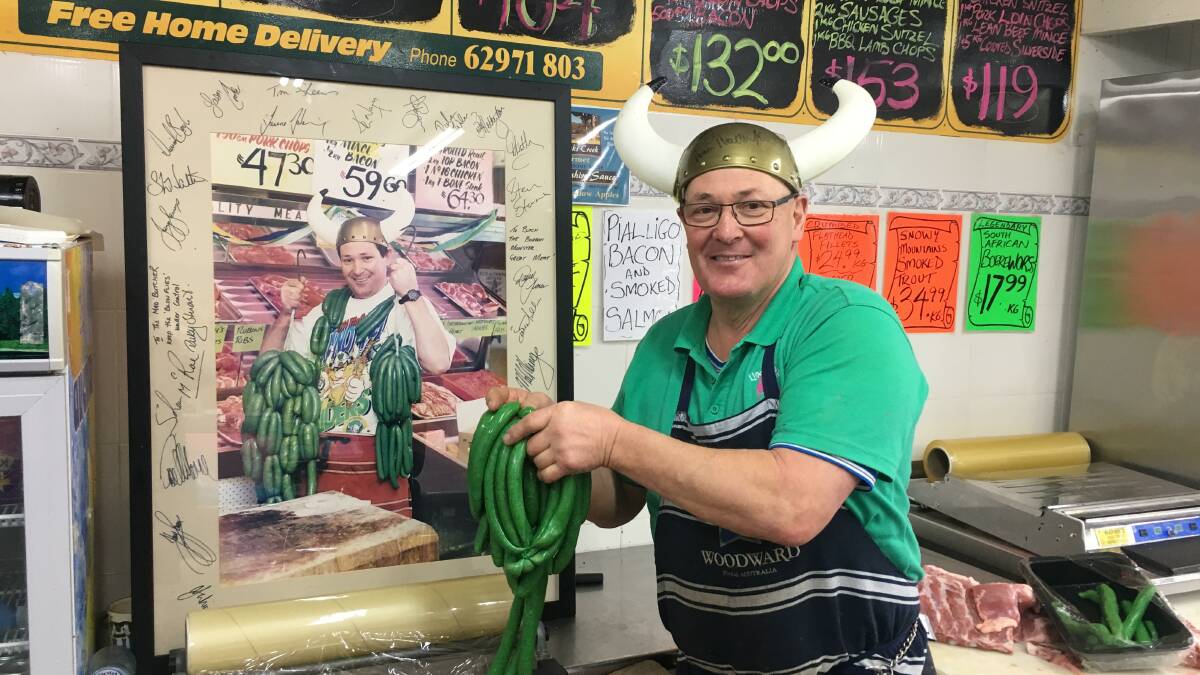 Peter "Butcher" Lindbeck with his famous green sausages. Behind him is his flashback to 1994, when the Raiders made the grand final. Picture: Peter Brewer