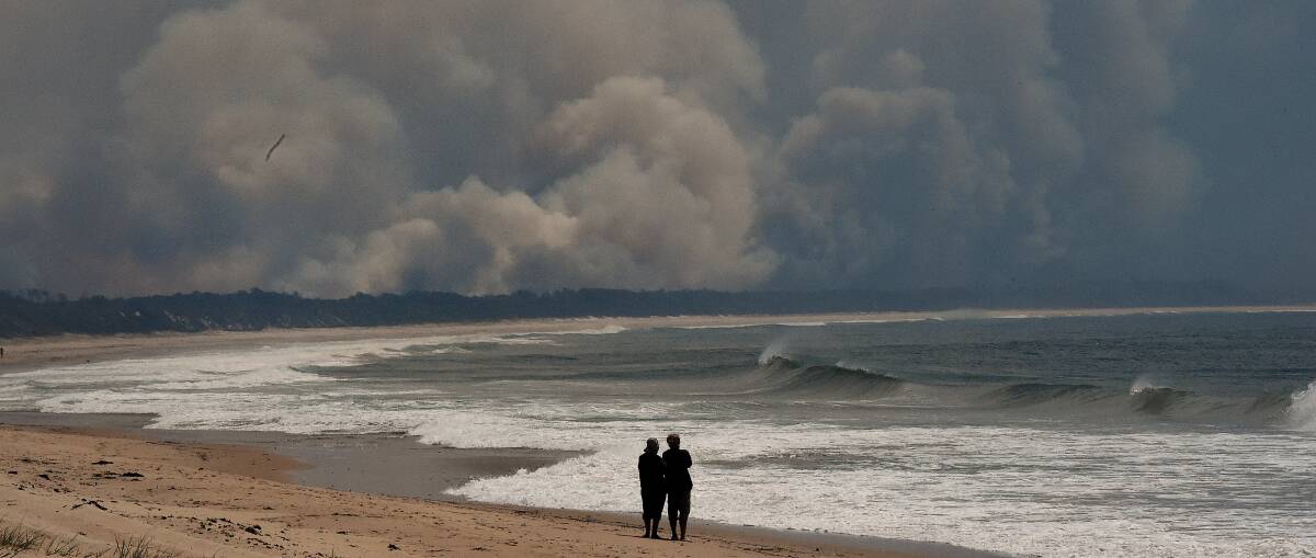 People stand on Diamond Beach watching smoke from bushfires in the Wallabi Point area fill the sky. Picture: Kate Geraghty