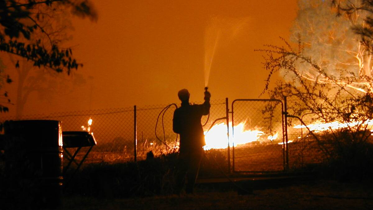 Gloria Jackson uses a garden hose to keep flames at bay behind her Kambah home during the 2003 Canberra bushfires. Picture: Malcom Harrington