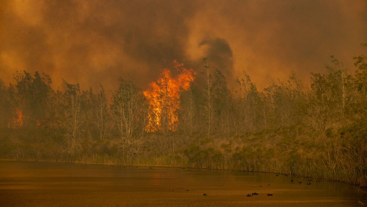 The bushfire jumps Willinga Lake before advancing into the heart of Bawley Point on December 5, 2019. Picture: Sitthixay Ditthavong