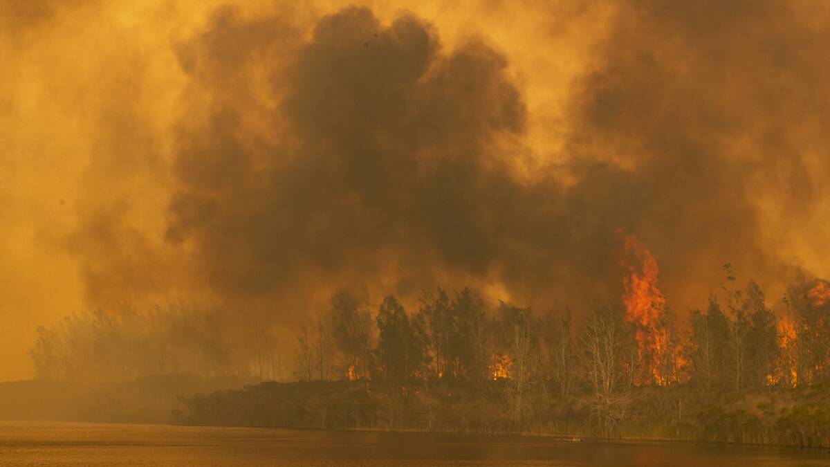 A bushfire jumps Willinga Lake at Bawley Point on Thursday. Picture: Sitthixay Ditthavong