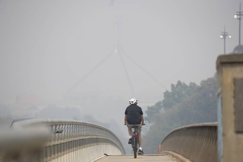 A cyclist rides over the Kings Avenue bridge as Parliament House is obscured by smoke haze. Picture: Sitthixay Ditthavong