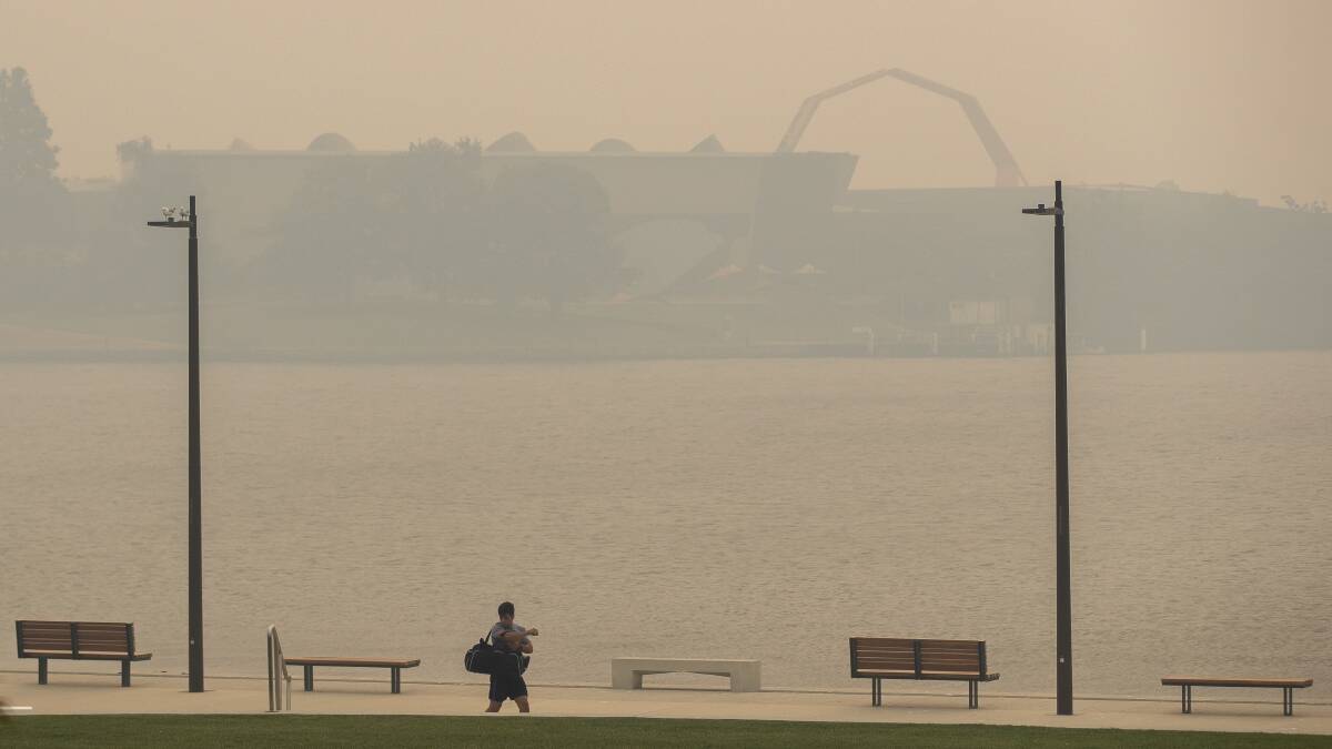 A man walks through Henry Rolland Park as the National Museum of Australia is obscured by smoke haze. Picture: Sitthixay Ditthavong