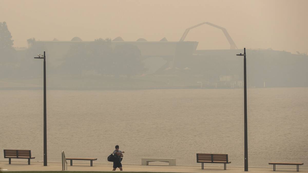A man walks through Henry Rolland Park on Tuesday afternoon as the National Museum of Australia is obscured by returning smoke haze in December 2019. Picture: Sitthixay Ditthavong 