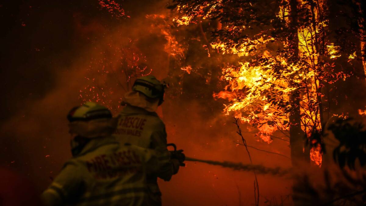 Fire and Rescue personal use a hose as they try to extinguish a bushfire as it burns near homes on the outskirts of the town of Bilpin on Thursday. Picture: Getty Images.
