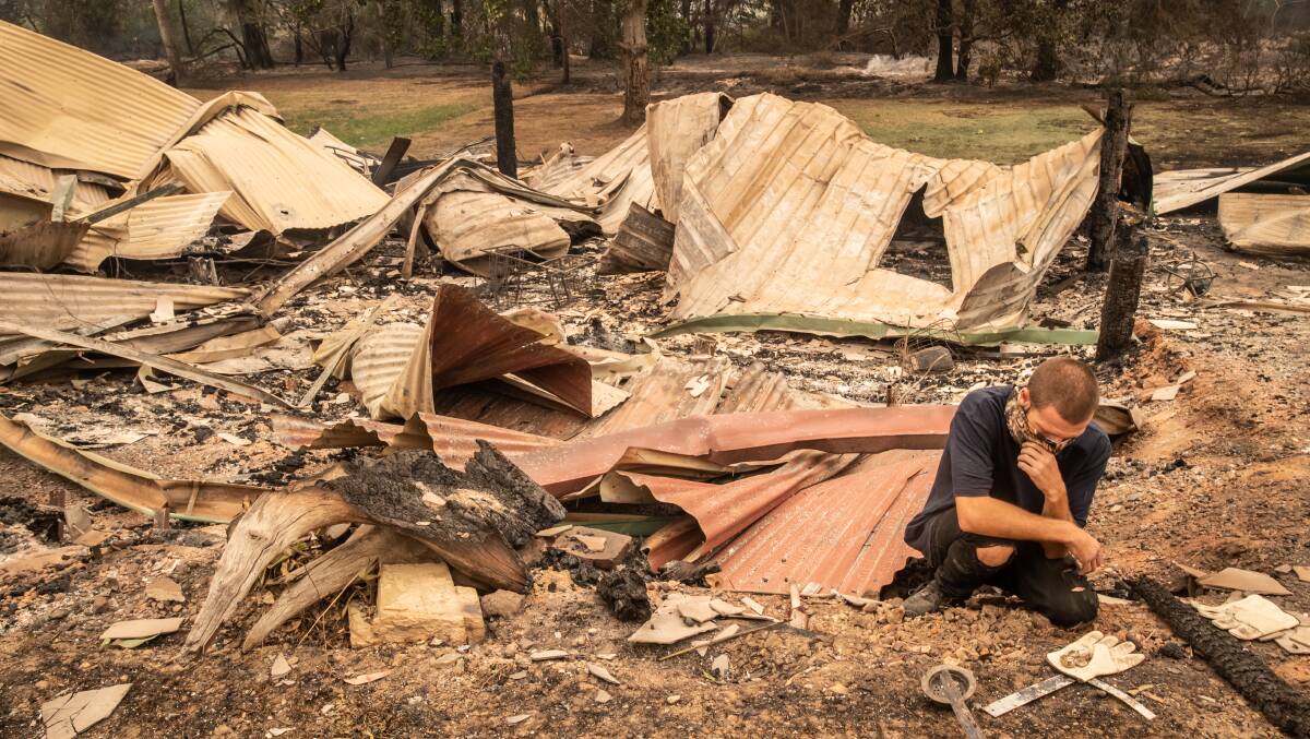 Karl Niehus sift through the wreckage after losing his businesses in Mogo to fires this week. Picture: Karleen Minney