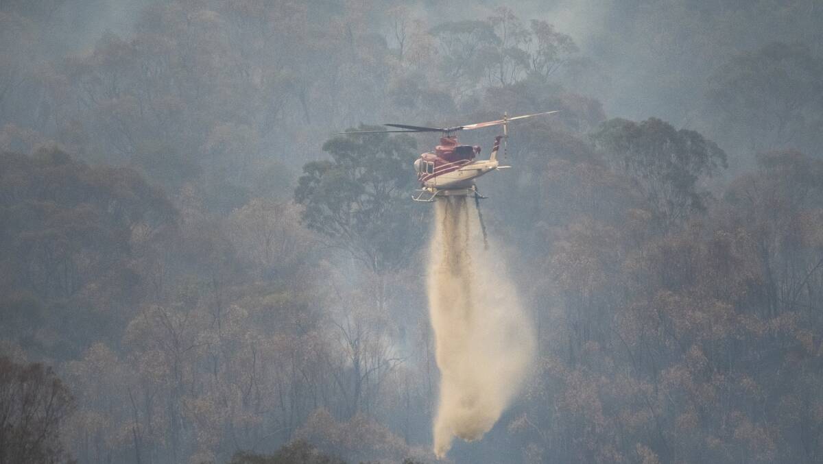 A helicopter drops water to slow the spread of the Orroral Fire, as seen from Naas Rd near Tharwa. Picture: Dion Georgopoulos