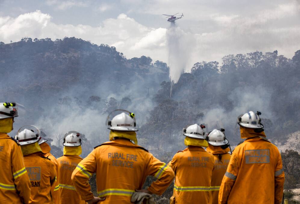 Fire crews watch as a helicopter is used to fight a fire threatening a properrty on Boboyan Road. Picture: Sitthixay Ditthavong