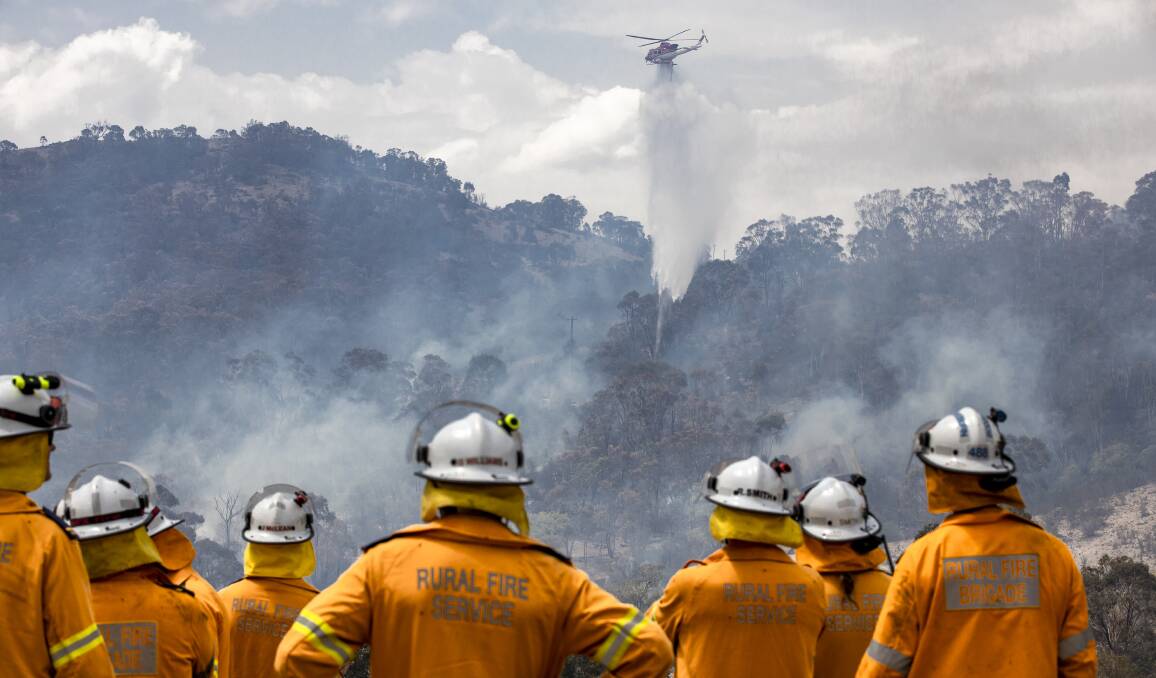 Fire crews watch as a helicopter is used to fight a fire threatening a property during the Orroral Valley bushfire. Picture: Sitthixay Ditthavong