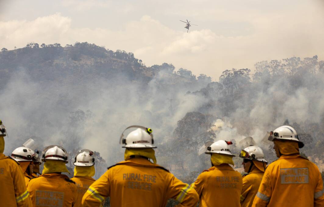 Fire crews watch as a helicopter is used to fight a fire threatening a property on Boboyan Road. Picture: Sitthixay Ditthavong