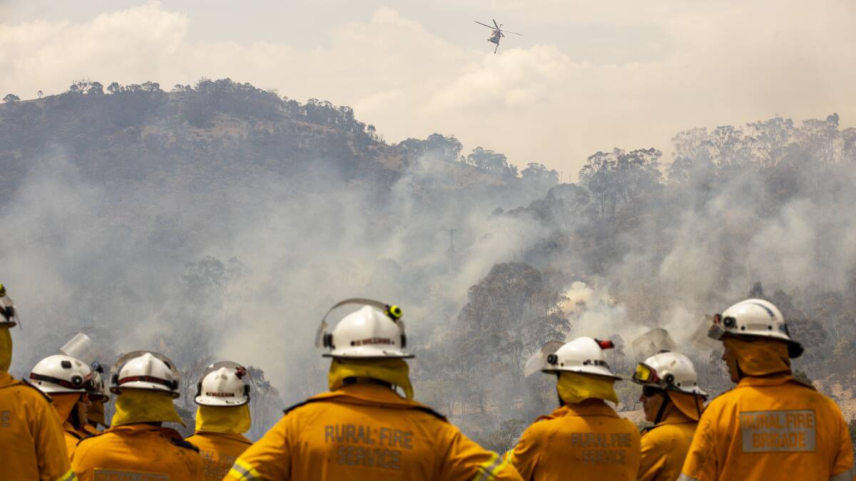 Fire crews watch as a helicopter is used to fight the Orroral Valley bushfire. Picture: Sitthixay Ditthavong