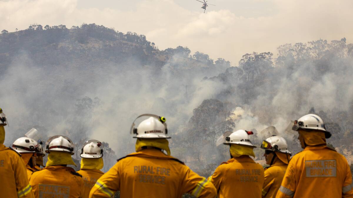 Fire crews watch as a helicopter is used to fight a fire threatening a properrty on Boboyan Road on Sunday afternoon. Picture: Sitthixay Ditthavong