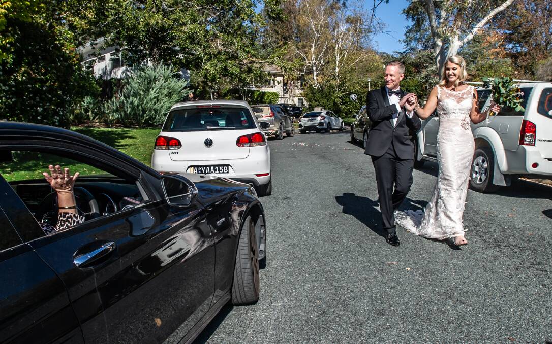 Former Olympic swimmer Dimity Douglas and her U.S.-born husband Douglas Boyd walk down the avenue of cars in Deakin containing their friends as they marry with coronavirus-era social distancing. Picture: Karleen Minney.