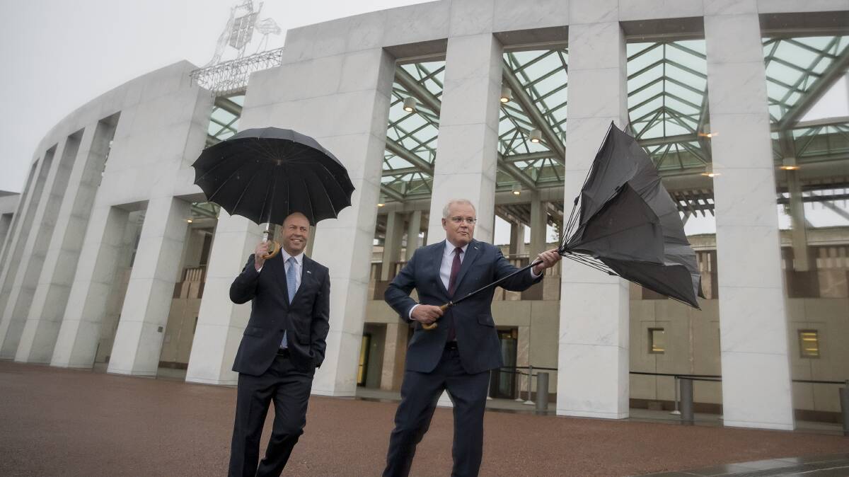 Treasurer Josh Frydenberg watches Prime Minister Scott Morrison struggle with an umbrella as they make their way to the front lawn of Parliament House to sell their budget to breakfast television networks in October. Picture: Sitthixay Ditthavong