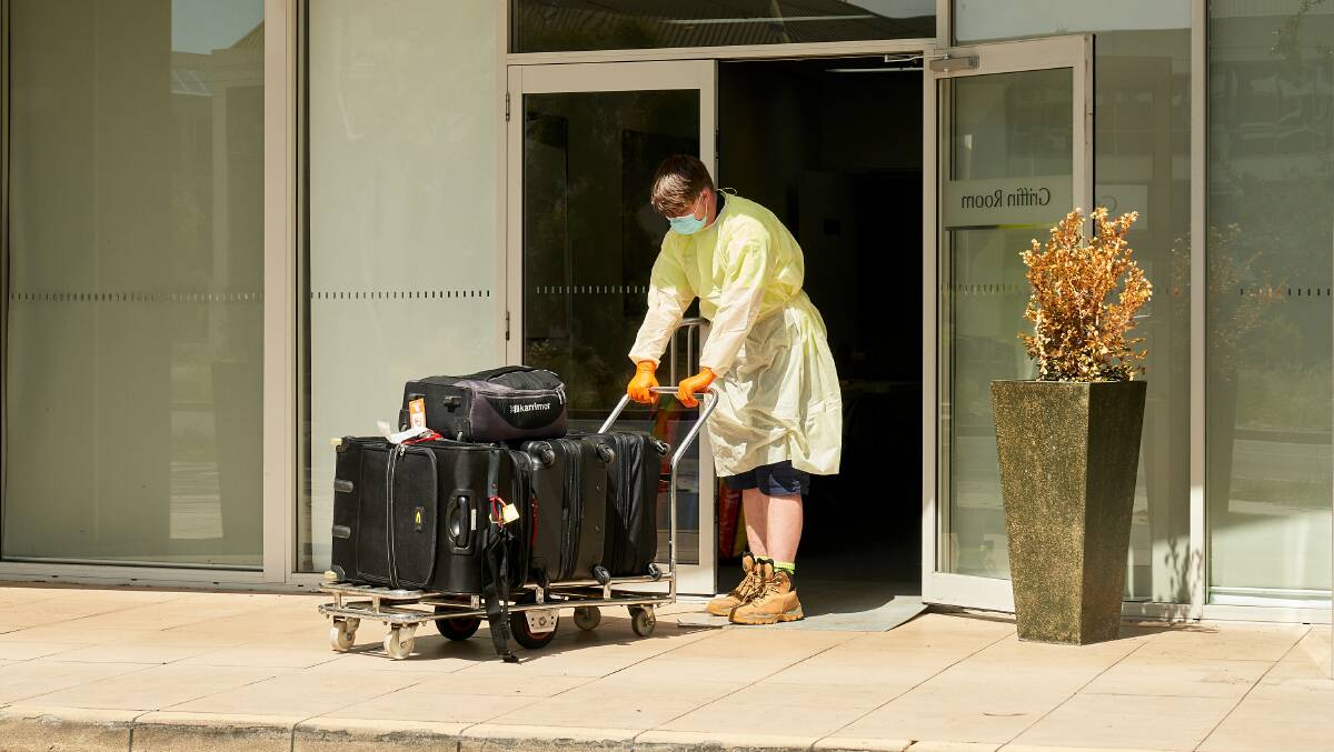 Travellers' luggage being moved by a staff member wearing personal protective equipment at the Pacific Suites Hotel in Braddon. Picture: Matt Loxton