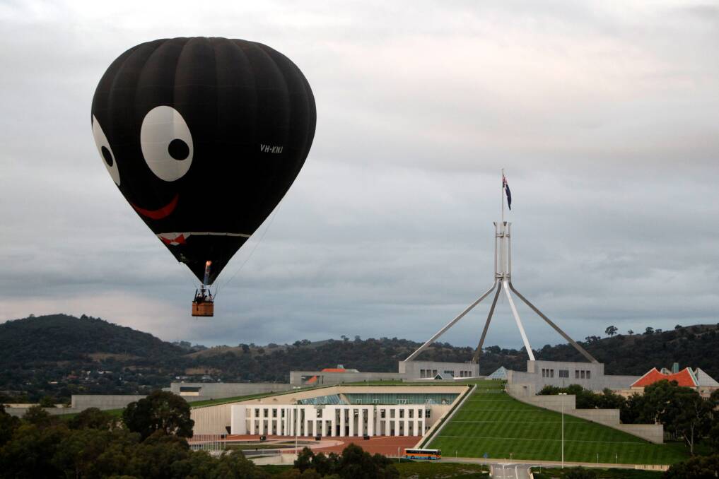 The Black Magic hot air balloon, also known as "Golly", is seen flying over Parliament House during the 2011 Canberra Balloon Spectacular. Photo: Alex Ellinghausen