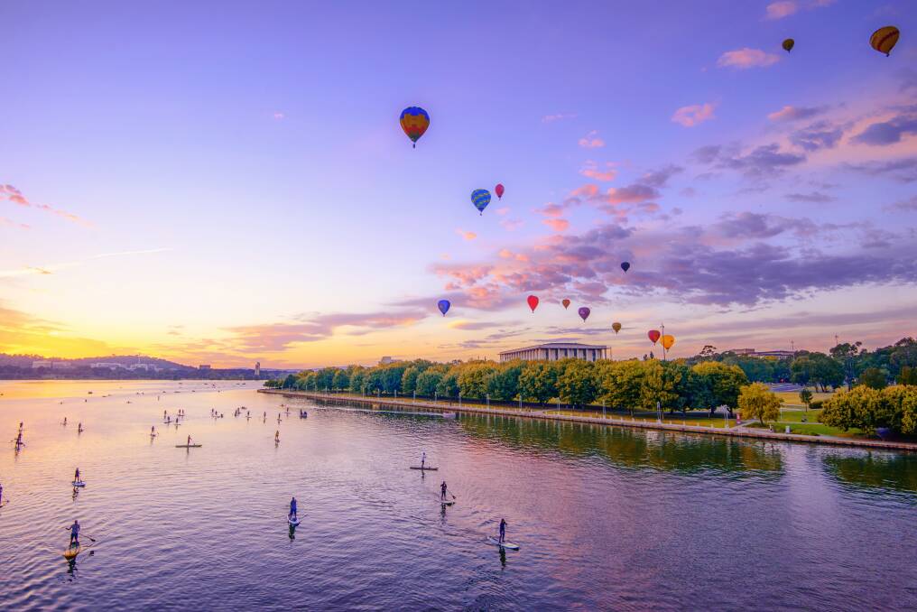 Balloons above the National Library as the sun rises over Lake Burley Griffin while paddle boarders take to the water. Photo: Carol Elvin