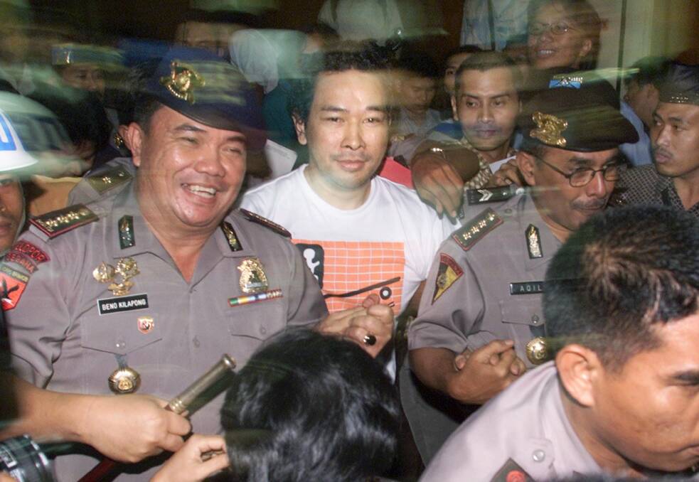 A police officer, left, smiles as he escorts Tommy, fugitive son of former Indonesian President Suharto, through a mob of reporters after his capture at police headquarters in Jakarta, Indonesia. Photo: AP