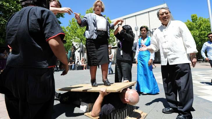 Minister Joy Burch helping promote an earlier Multicultural festival - by standing on Kung Fu grandmaster Neal Hardy before a world record attempt that had him lie on a bed of nails with more than 500kg of bricks placed on his torso. Photo: Andrew Sheargold