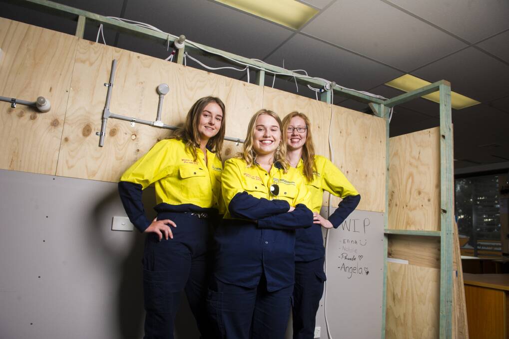 Electrical apprentices Phoebe Thompson, Elina Ulrich and Natalie Fowler in front of a frame they built and wired during training. Photo: Dion Georgopoulos