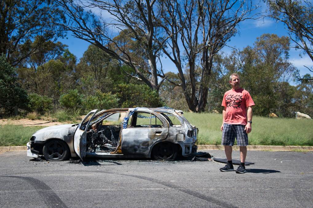Fraser resident Tony Baker standing beside a burnt out Nissan Pulsar in the Wickens Place car park, where many cars are torched. Photo: Elesa Kurtz