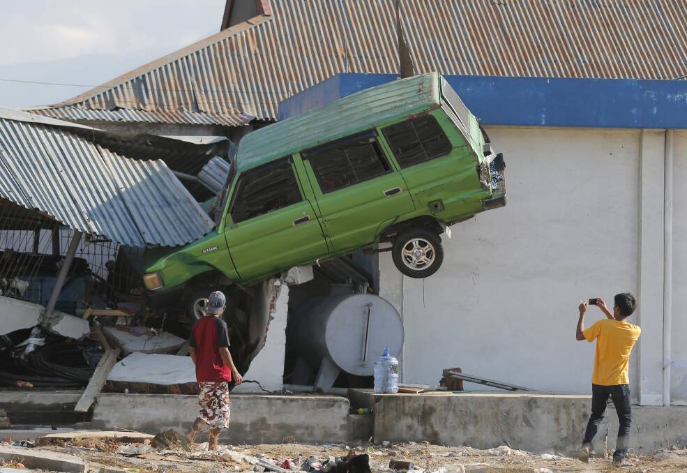 A man takes a photo of a car lifted into the air by the tsunami at Talise beach in Palu, Photo: AP