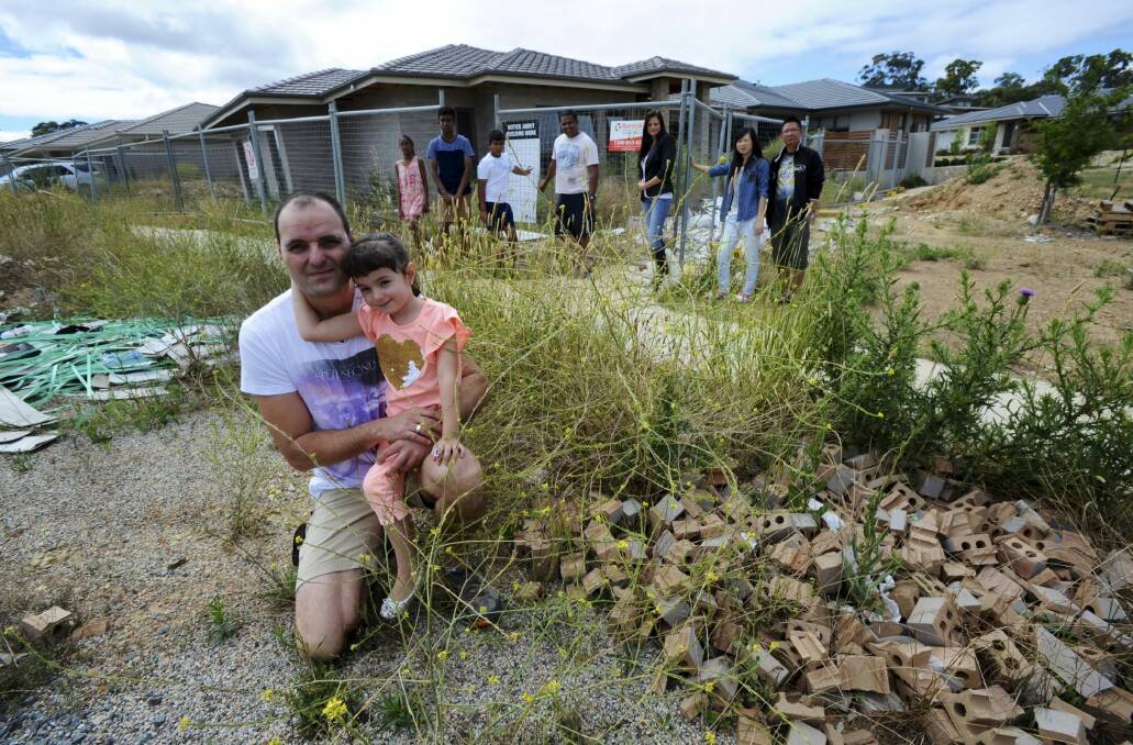Neighbours say this abandoned building site in Crace is an "accident waiting to happen". At front are Ivan Coric and his daughter,
Katija. At rear from left, Nethmi, Kaveen, Deshan and Kanchana
Marasinghe, Anisa Coric, Rachel Huang and Yuandong Zhong. Photo: Graham Tidy