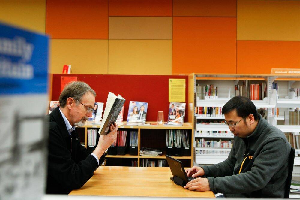 Tim Atkinson reads at the library while Li Weimin uses the free WiFi. CCTV cameras at ACT public libraries will be upgraded and computer terminals are set to change. Photo: Katherine Griffiths
