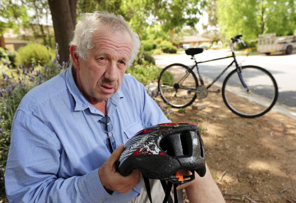 Brian Pearce, 60, shows his split helmet and damaged bicycle outside his Tuggeranong home.  Photo: Graham Tidy 