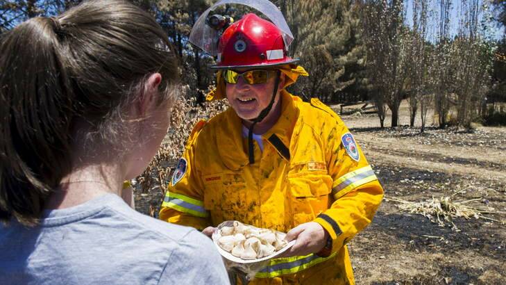 Bungendore RFS Captain, Sheldon Williams, accepts a plate of home-made meringues from Jacqui Coleman after extinguishing a burning stump at a property next to the Kings Highway near Bungendore. Photo: Rohan Thomson