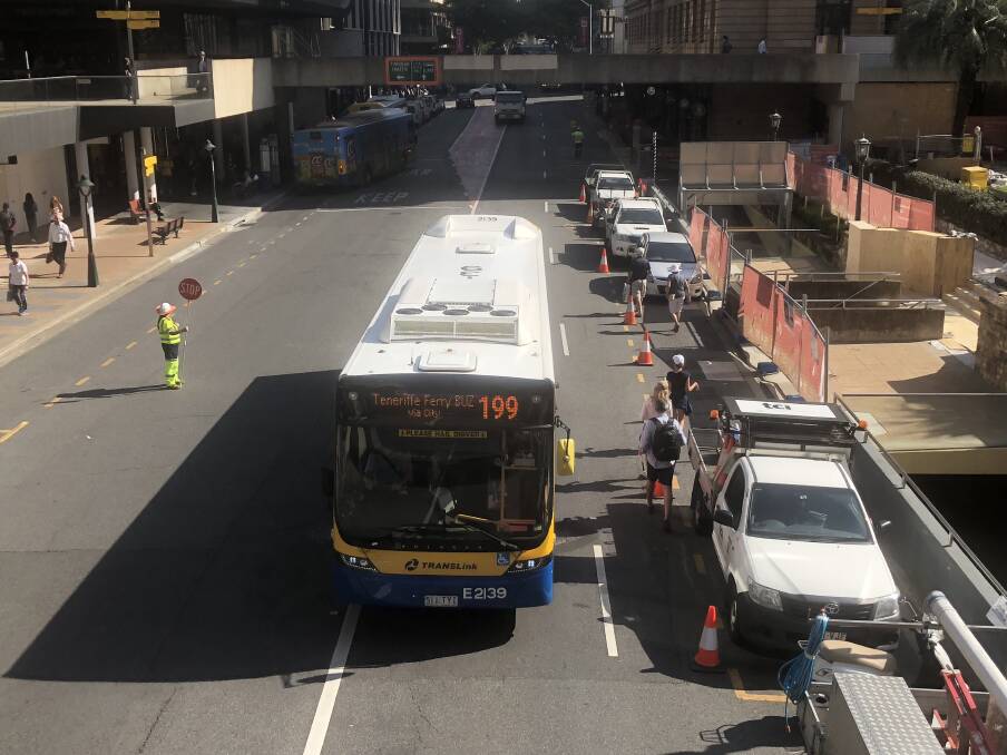 Pedestrians walking between parked vehicles and a bus on Adelaide Street. Photo: Ruth McCosker