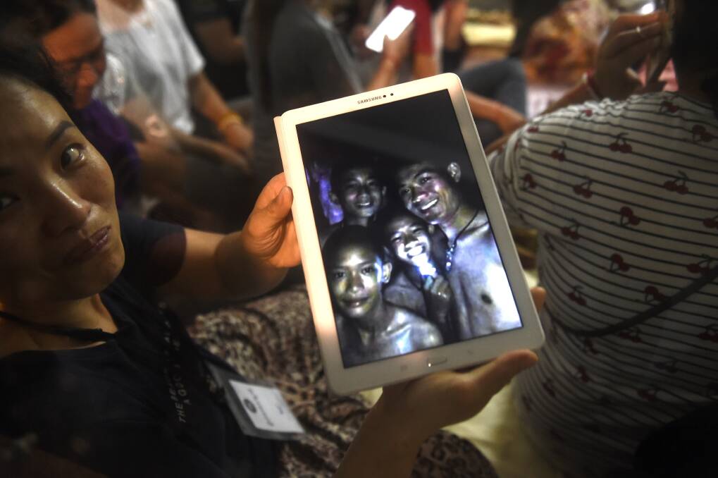 Thanaporn Promthep displays an image of her missing son Duangpetch (second right) and his coach “Ek” (right). Photo: AFP