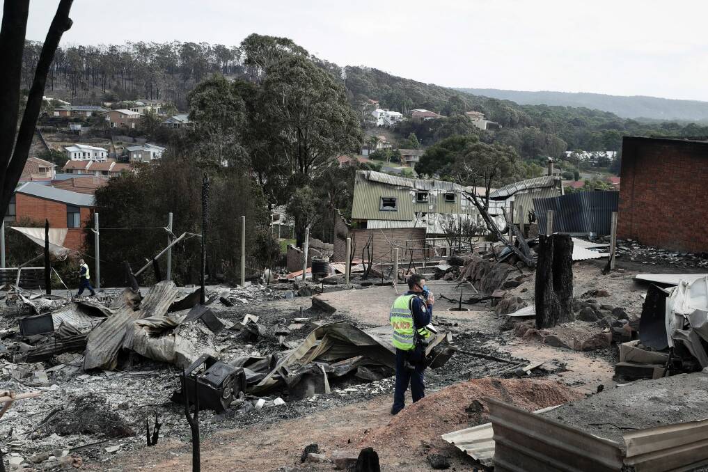 A police officer takes photos of the aftermath of the Tathra bushfires, which destroyed 68 homes. Photo: Alex Ellinghausen