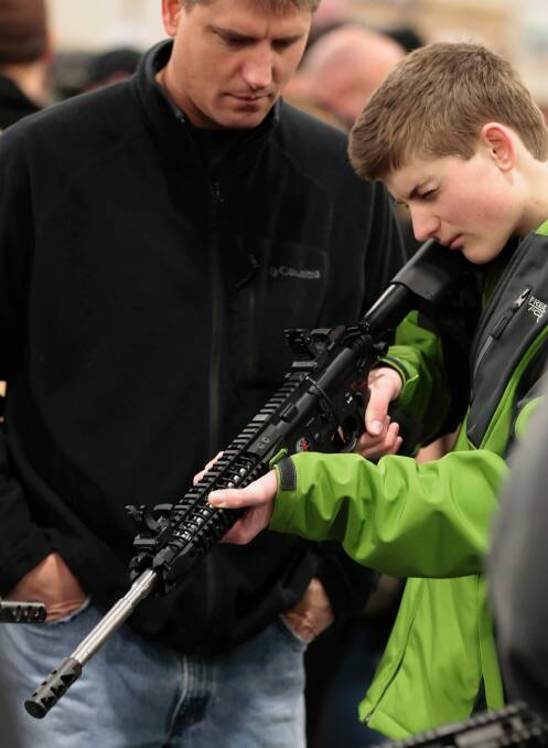 A boy holds a semi-automatic assault rifle while his father watches at a Utah gun show. Photo: George Frey