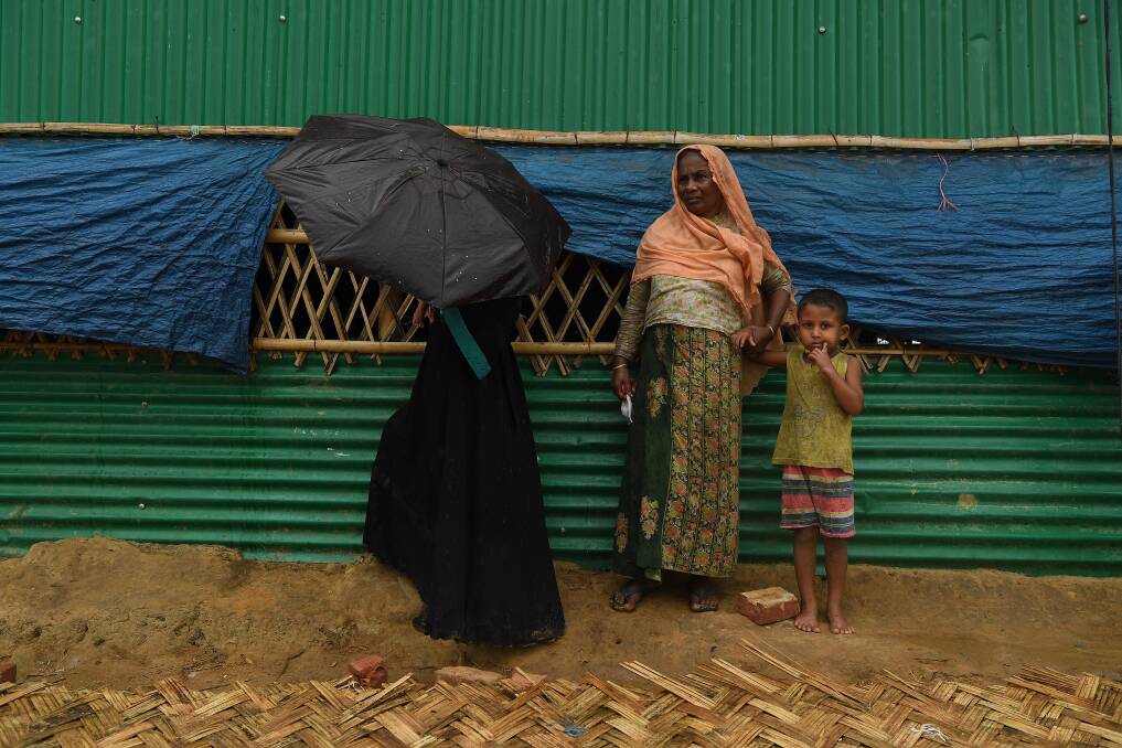 Rohingya women take shelter during a monsoonal downpour in Hakim Para Camp this week. Photo: Kate Geraghty