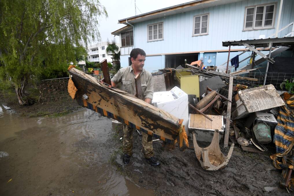 A man helps strangers remove flood-damaged items from their home in the Townsville suburb of Rosslea on Thursday. Photo: Dan Peled - AAP