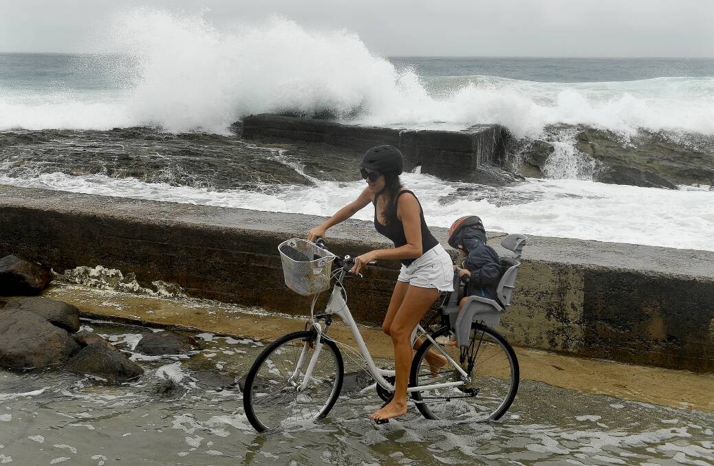 A woman negotiates a flooded path at Snapper Rocks on the Gold Coast as huge swells and high tides are set to pummel south-east Queensland and far-northern New South Wales beaches over the coming days. Photo: AAP/Dave Hunt