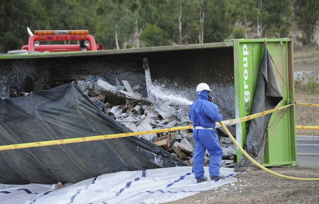 A worker hoses down the rubble spilling from the truck. Photo: Graham Tidy